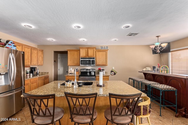 kitchen with stainless steel appliances, a breakfast bar, a sink, visible vents, and a center island with sink