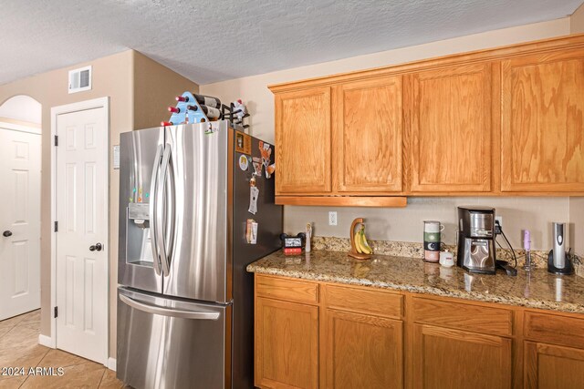 kitchen with stone counters, arched walkways, visible vents, a textured ceiling, and stainless steel fridge