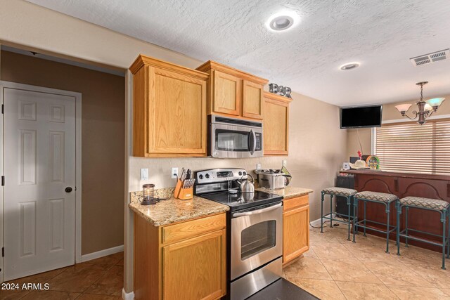 kitchen featuring visible vents, appliances with stainless steel finishes, a textured ceiling, a chandelier, and baseboards