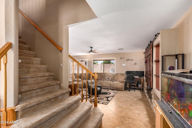 living area with light tile patterned floors, ceiling fan, a barn door, and stairway