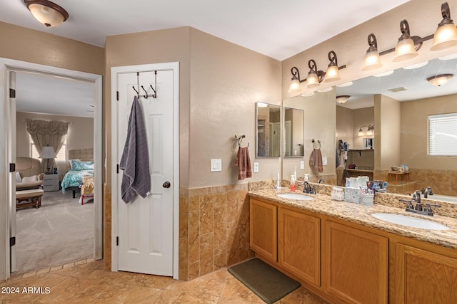 ensuite bathroom featuring ensuite bathroom, double vanity, a sink, and tile walls