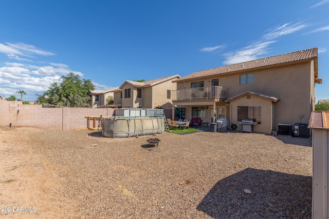 back of house with a fenced backyard, a balcony, central air condition unit, a fenced in pool, and stucco siding