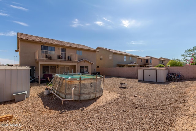 back of house with a fenced backyard, an outdoor structure, a balcony, and a storage unit