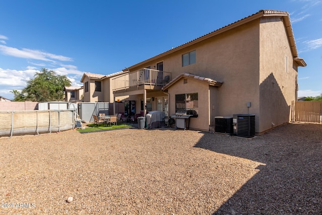 back of property with a balcony, a fenced backyard, central AC, and stucco siding