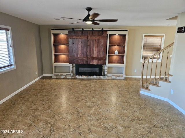 unfurnished living room featuring visible vents, a glass covered fireplace, ceiling fan, baseboards, and stairs