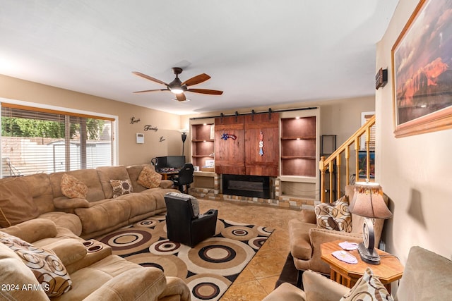 living room featuring a barn door, a glass covered fireplace, ceiling fan, tile patterned floors, and stairs