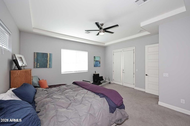 carpeted bedroom with ceiling fan, multiple windows, and a tray ceiling