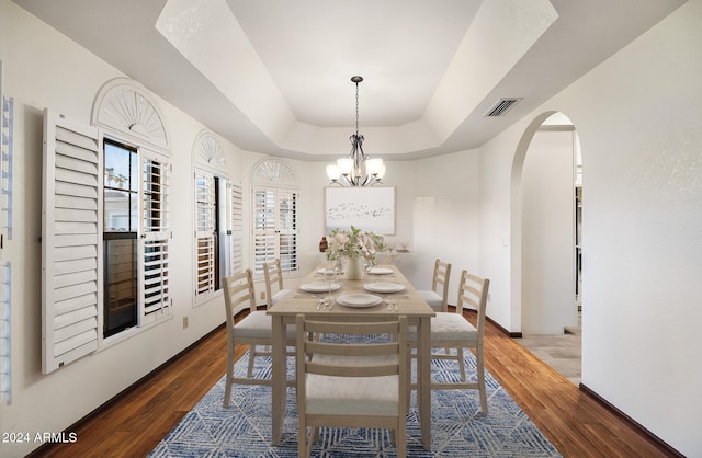 dining room featuring a notable chandelier, dark wood-type flooring, and a tray ceiling