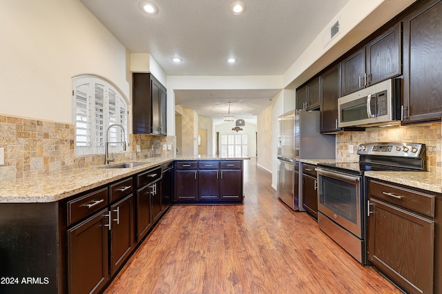 kitchen with kitchen peninsula, appliances with stainless steel finishes, decorative backsplash, sink, and hardwood / wood-style floors