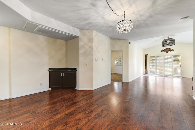 unfurnished living room with dark wood-type flooring, lofted ceiling, and a notable chandelier