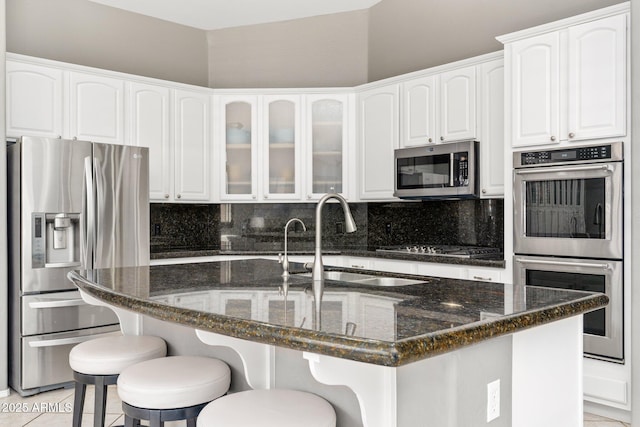 kitchen with tasteful backsplash, appliances with stainless steel finishes, dark stone counters, and a sink