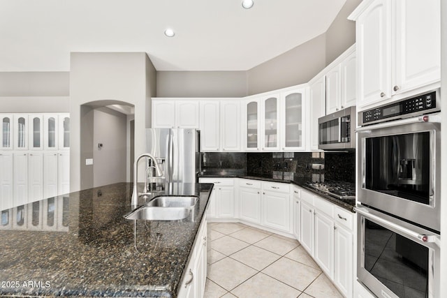 kitchen with light tile patterned floors, tasteful backsplash, appliances with stainless steel finishes, glass insert cabinets, and a sink