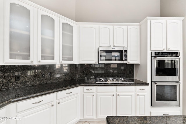 kitchen with white cabinets, appliances with stainless steel finishes, decorative backsplash, and dark stone countertops