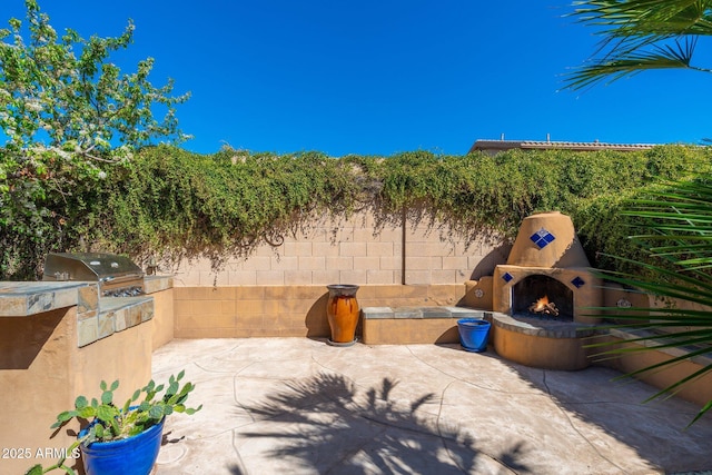 view of patio / terrace with fence, a lit fireplace, and area for grilling