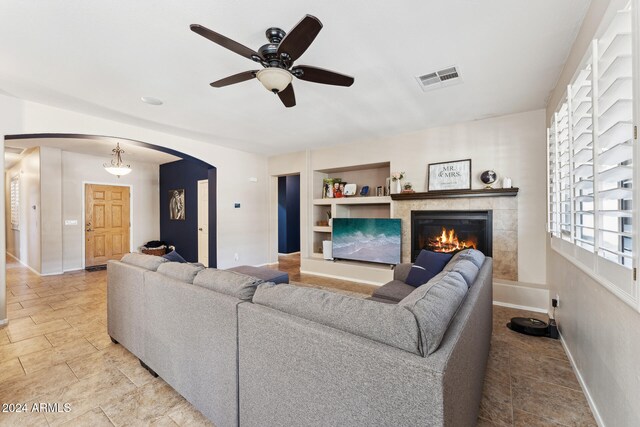 living room featuring ceiling fan, a tiled fireplace, and built in shelves