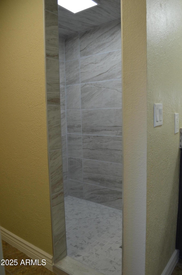 full bathroom featuring a textured wall, a tile shower, and baseboards