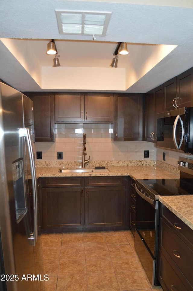 kitchen featuring a tray ceiling, decorative backsplash, appliances with stainless steel finishes, dark brown cabinetry, and a sink