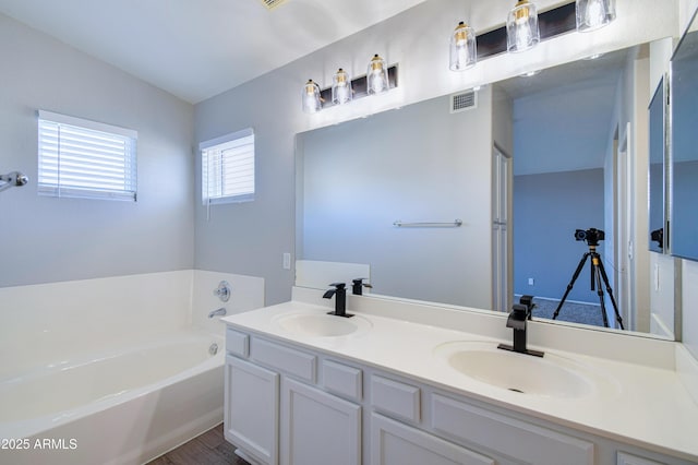 full bathroom with double vanity, a garden tub, visible vents, and a sink