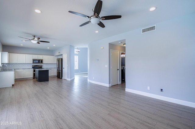 unfurnished living room with light wood-type flooring, a sink, visible vents, and baseboards