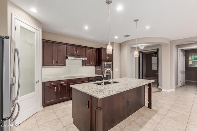 kitchen with a sink, appliances with stainless steel finishes, under cabinet range hood, arched walkways, and light tile patterned flooring