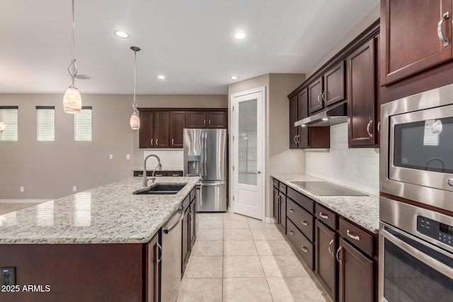 kitchen with stainless steel appliances, a sink, tasteful backsplash, a center island with sink, and under cabinet range hood