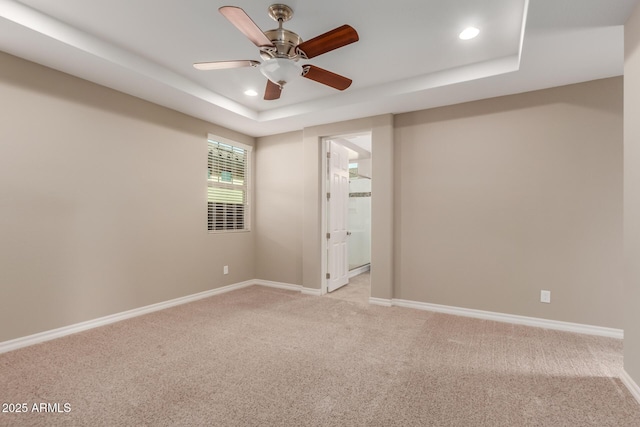 empty room with a tray ceiling, recessed lighting, light colored carpet, baseboards, and a ceiling fan