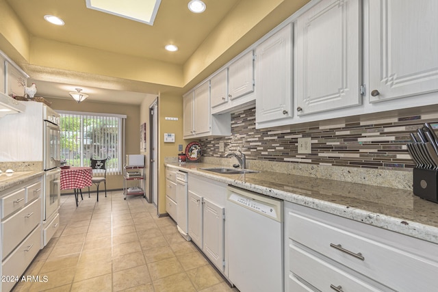 kitchen featuring light stone countertops, sink, white cabinetry, white dishwasher, and light tile patterned floors