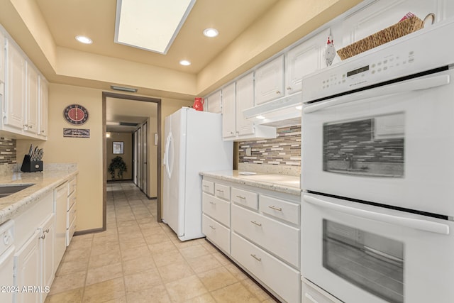 kitchen with white appliances, ventilation hood, light stone counters, backsplash, and white cabinetry