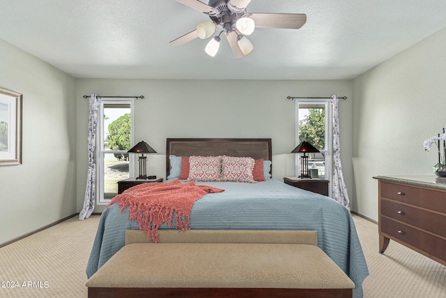 bedroom featuring a textured ceiling, multiple windows, ceiling fan, and light colored carpet