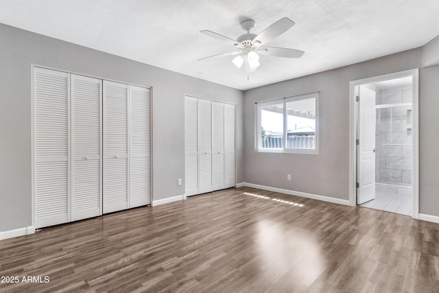 unfurnished bedroom featuring two closets, baseboards, and wood finished floors