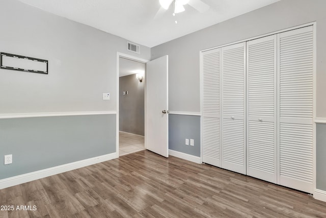 unfurnished bedroom featuring a closet, visible vents, baseboards, wood finished floors, and a ceiling fan