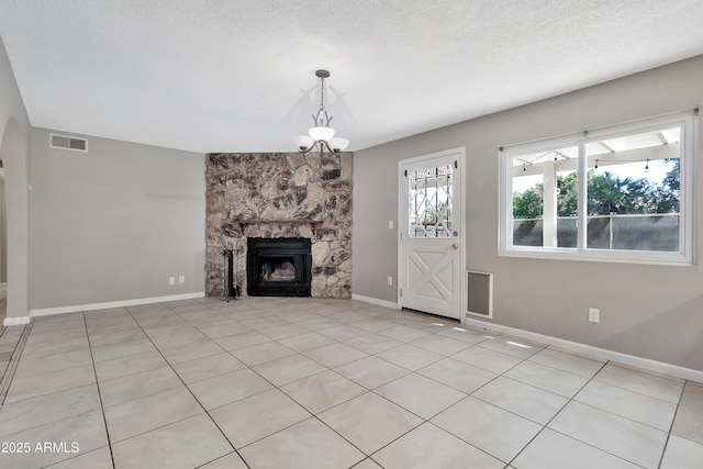 unfurnished living room featuring a textured ceiling, visible vents, baseboards, a fireplace, and an inviting chandelier