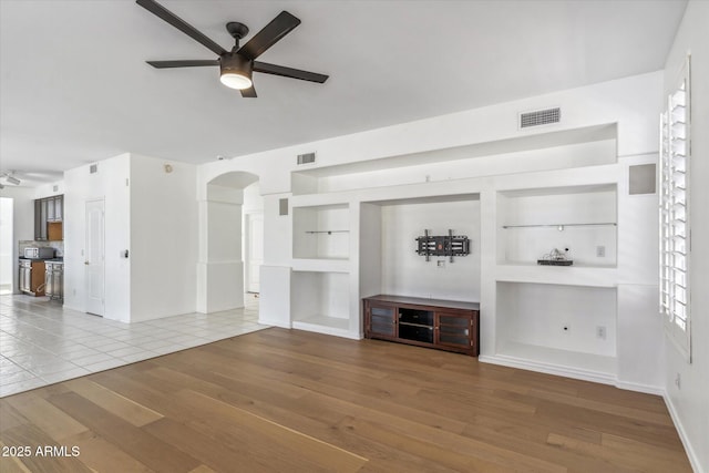 unfurnished living room featuring hardwood / wood-style flooring, ceiling fan, and built in shelves