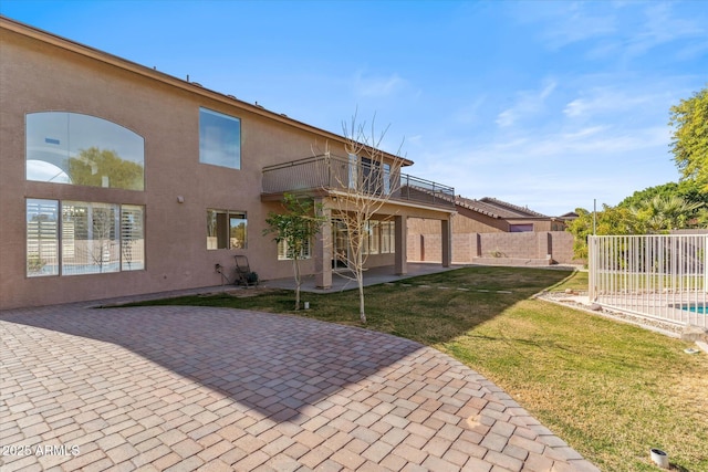 rear view of property featuring a balcony, a yard, and a patio