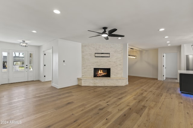 unfurnished living room with a stone fireplace, ceiling fan, and light wood-type flooring