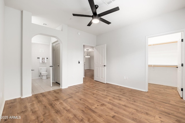 unfurnished bedroom featuring light wood-style floors, visible vents, arched walkways, and ensuite bathroom