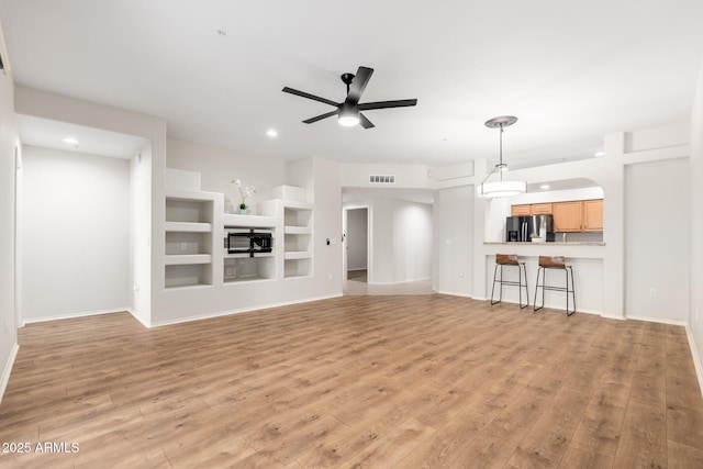 unfurnished living room with baseboards, visible vents, a ceiling fan, light wood-type flooring, and built in shelves