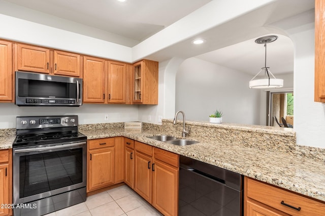 kitchen with a sink, appliances with stainless steel finishes, light stone countertops, brown cabinetry, and decorative light fixtures