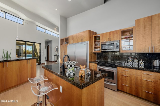 kitchen featuring a kitchen breakfast bar, a towering ceiling, stainless steel appliances, light hardwood / wood-style flooring, and a center island