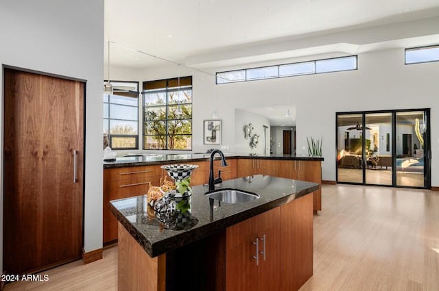 kitchen with a center island with sink, sink, dark stone counters, and light hardwood / wood-style flooring