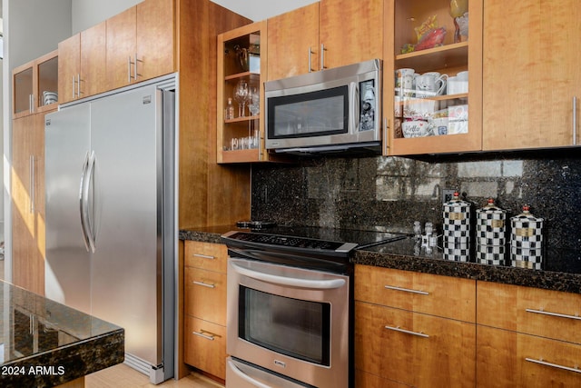 kitchen with appliances with stainless steel finishes, backsplash, light hardwood / wood-style flooring, and dark stone counters