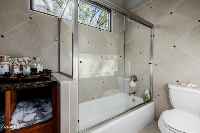 bathroom featuring shower / bath combination with glass door, toilet, and tile walls