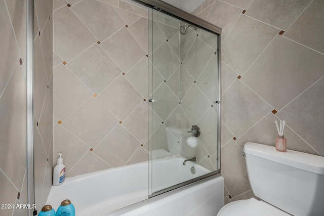 bathroom with toilet, bath / shower combo with glass door, and tile walls