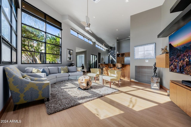 living room featuring ceiling fan, a high ceiling, and light wood-type flooring