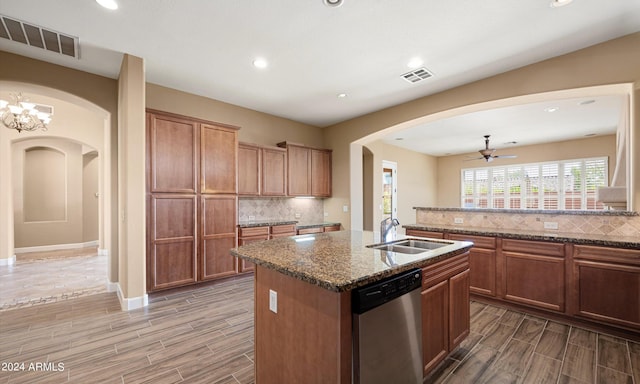 kitchen featuring sink, a center island with sink, dishwasher, dark stone counters, and decorative backsplash