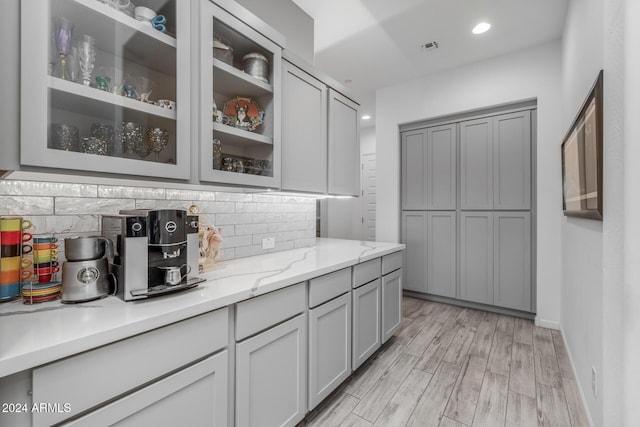 kitchen featuring backsplash, gray cabinets, light stone countertops, and light hardwood / wood-style flooring