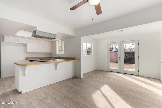 kitchen featuring white cabinetry, a kitchen bar, kitchen peninsula, light wood-type flooring, and french doors