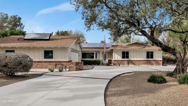 ranch-style house featuring brick siding, concrete driveway, board and batten siding, roof mounted solar panels, and a garage