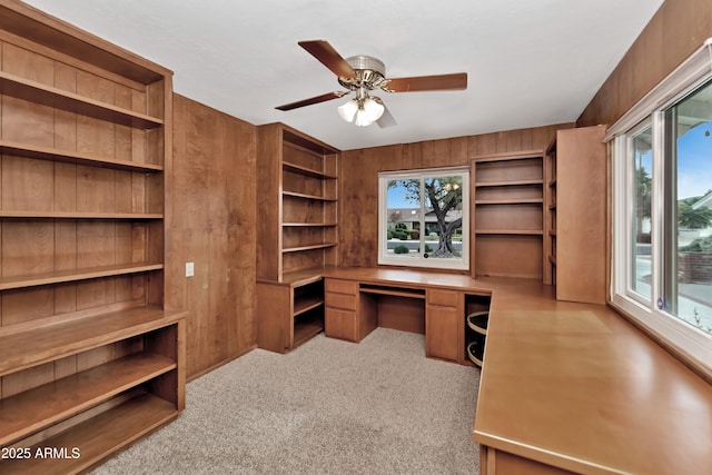 carpeted home office with wooden walls, a healthy amount of sunlight, and built in desk