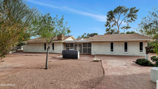 view of front of property featuring a shingled roof, a patio area, a chimney, and stucco siding